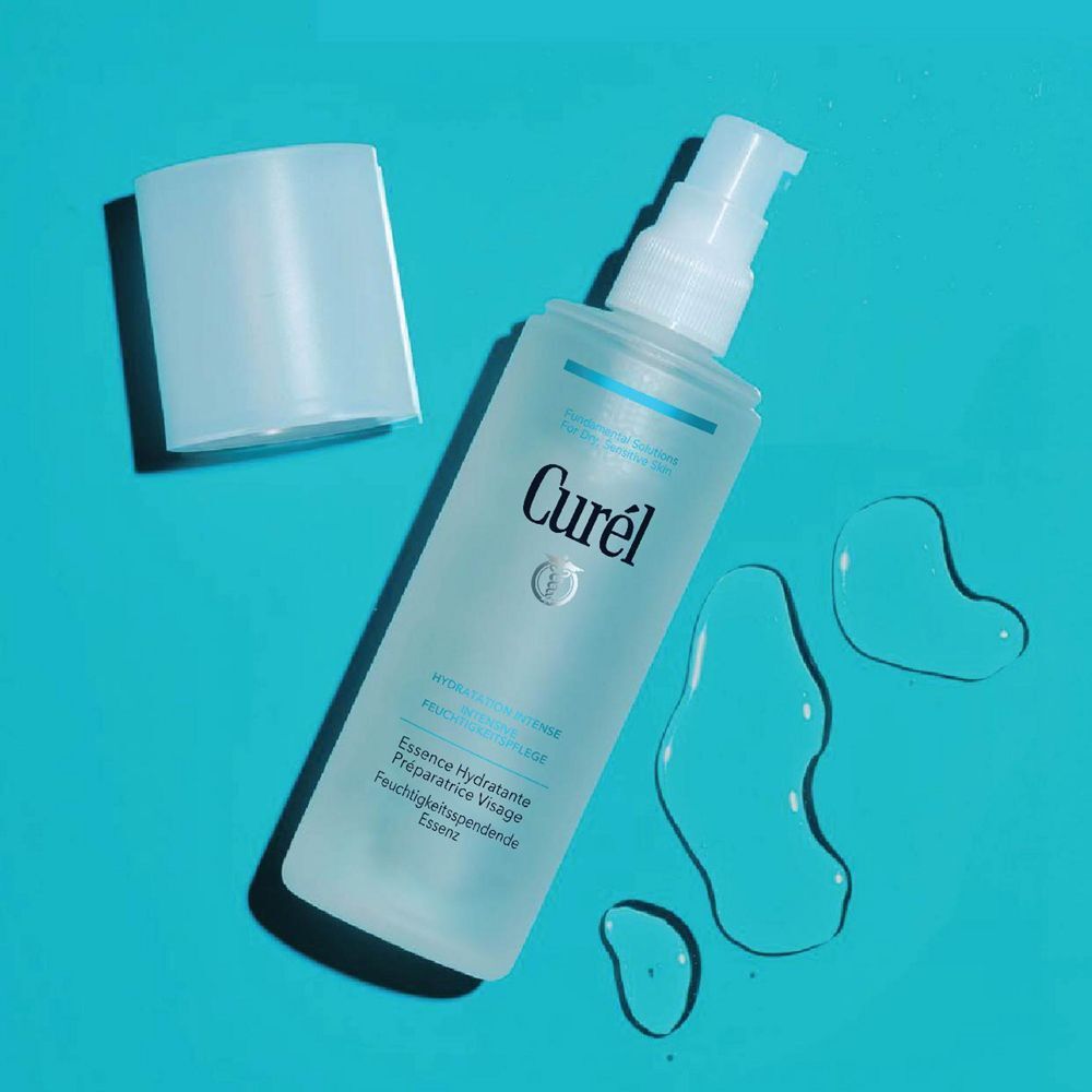 Curél Feuchtigkeitsspendende Essenz. Transparente Flasche mit weißem Pumpkopf. Blaue Flüssigkeit daneben. Text: Curél, Essenz.
