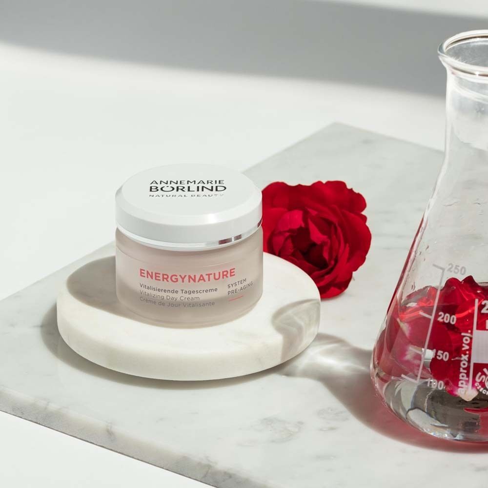 Tiegel ANNEMARIE BÖRLIND ENERGY NATURE Vitalisierende Tagescreme neben einer Rose und einem Becherglas.
