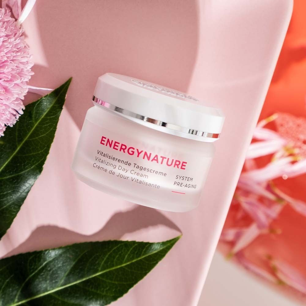 Tiegel ANNEMARIE BÖRLIND ENERGY NATURE Vitalisierende Tagescreme auf rosa Unterlage mit Blättern.