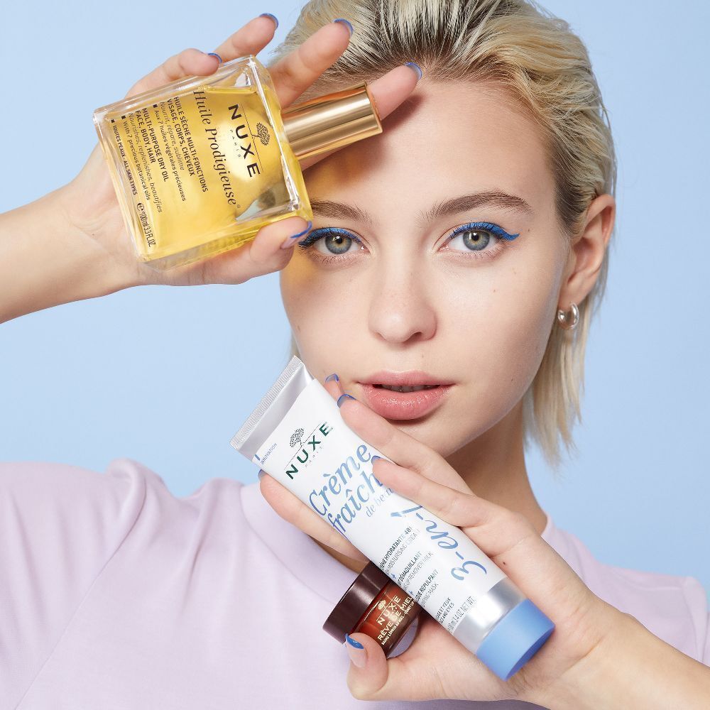 Frau hält Produkte: Crème Fraîche de Beauté, Öl und Creme. Weiß, blau. 3-en-1 Feuchtigkeitspflege.