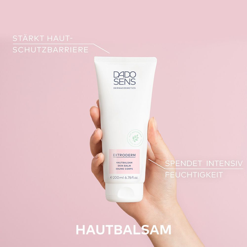 Hand hält eine Tube DADO SENS EXTRODERM Hautbalsam vor rosafarbenem Hintergrund.
