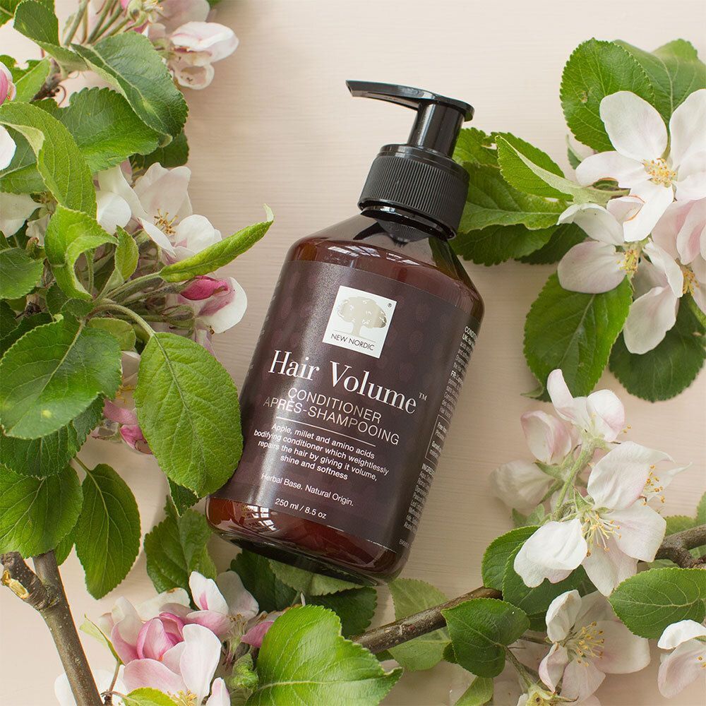 Flasche NEW NORDIC Hair Volume™ Conditioner, umgeben von Blüten. Braune Flasche mit schwarzem Pumpverschluss.
