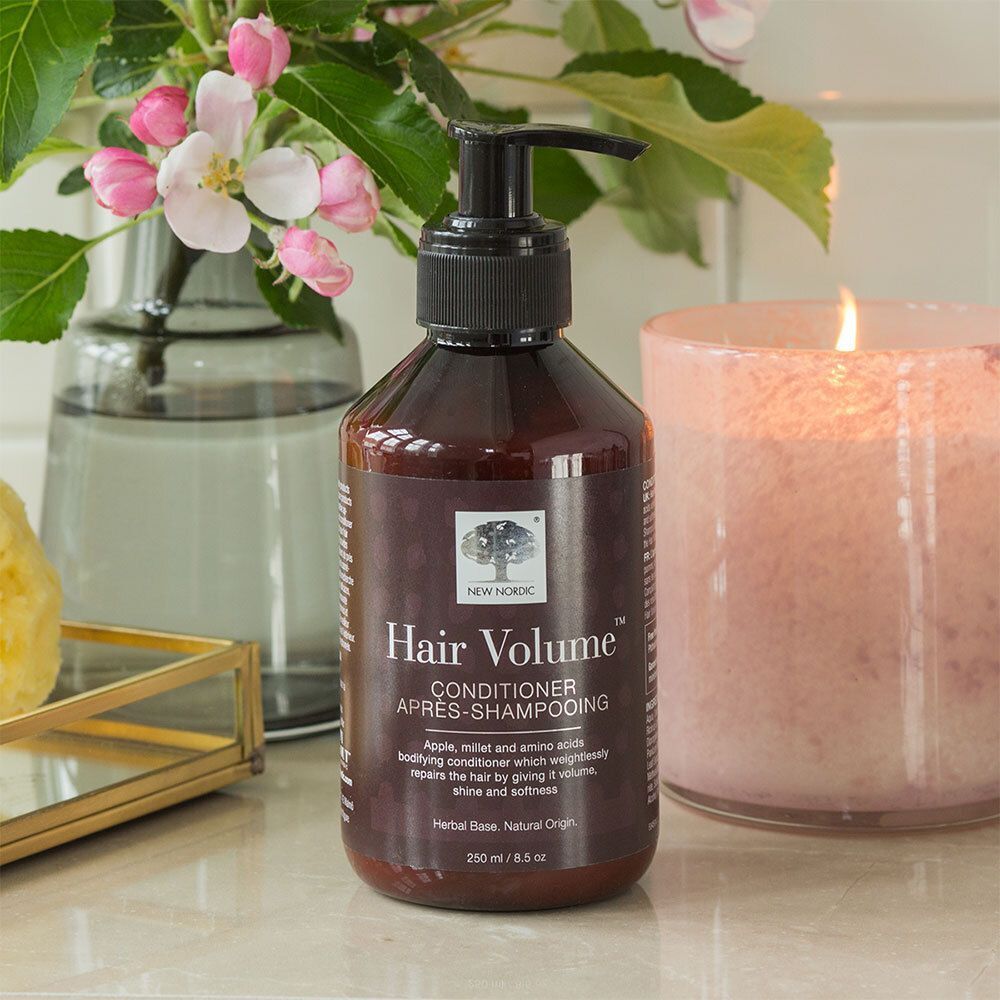 Flasche NEW NORDIC Hair Volume™ Conditioner neben einer Kerze und einem Glas. Braune Flasche mit schwarzem Pumpverschluss.