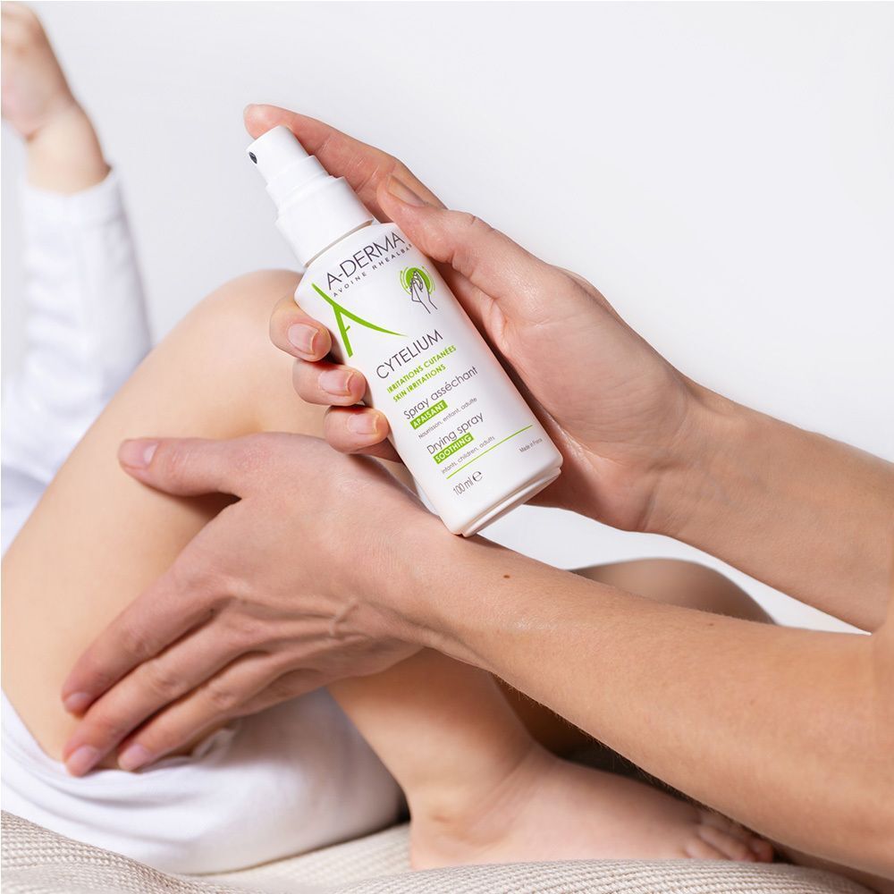 Person hält A-DERMA CYTELIUM Spray auf dem Bein eines Kindes. Produktetikett sichtbar.