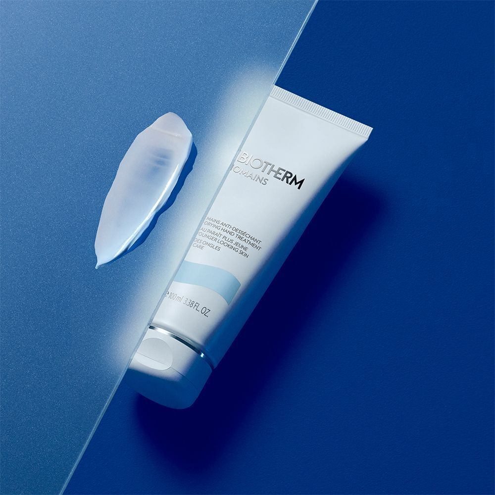 BIOTHERM Biomains Handcreme-Tube und eine Creme-Probe auf blauem Hintergrund. Aufschrift: Anti-Desséchant Hand Treatment, für jünger aussehende Haut.