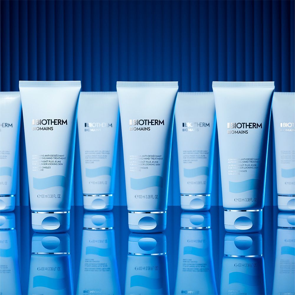 Reihe von BIOTHERM Biomains Handcreme-Tuben. Aufschrift: Anti-Desséchant Hand Treatment, für jünger aussehende Haut, Nagelpflege. Hintergrund: blau.