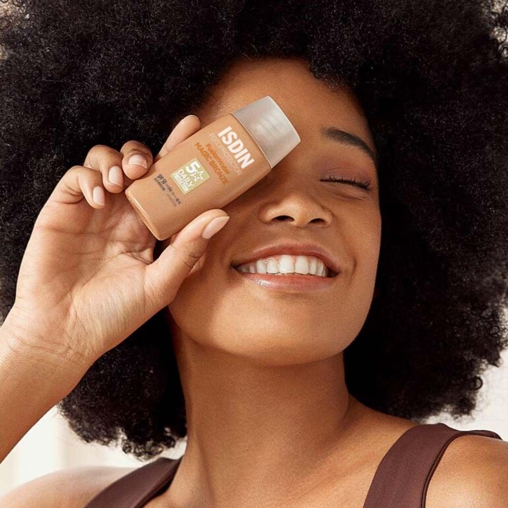 Frau hält ISDIN Fusion Water Magic Bronze vor dem Auge. Aufschrift: 5 Daily Protection.