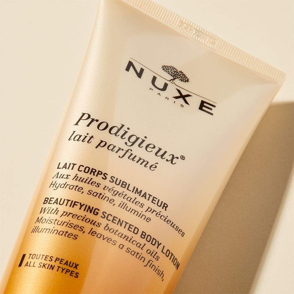 Nahaufnahme einer goldfarbenen Tube. Produktname und Logo sichtbar. Text: "Prodigieux lait parfumé".