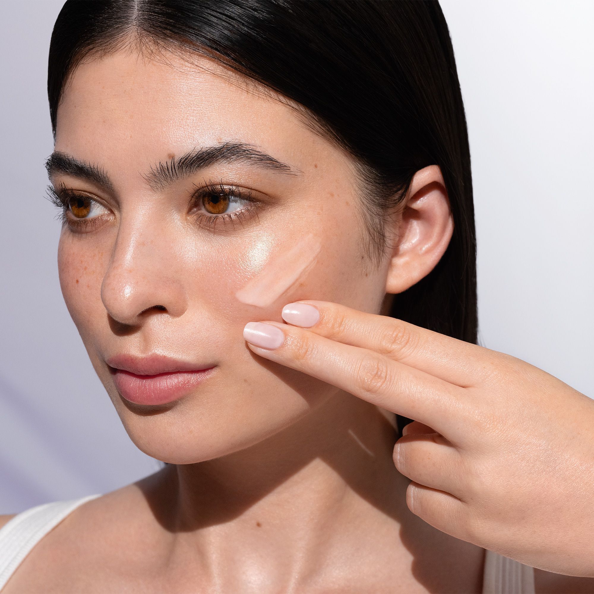 Eine Frau trägt ANNEMARIE BÖRLIND NATU COLLAGEN BOOST Gesichtsfluid auf ihre Wange auf.