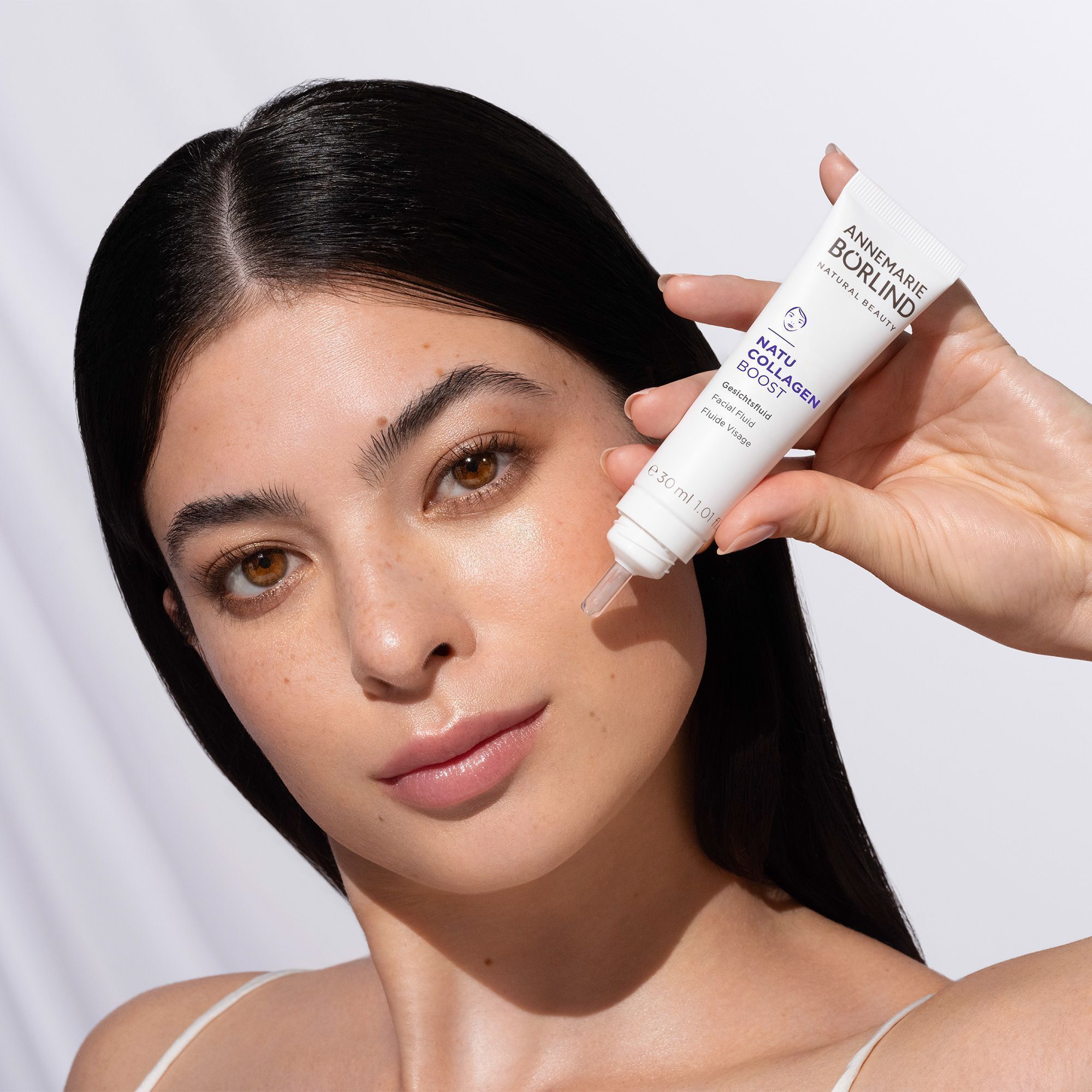 Eine Frau hält eine Tube ANNEMARIE BÖRLIND NATU COLLAGEN BOOST Gesichtsfluid.