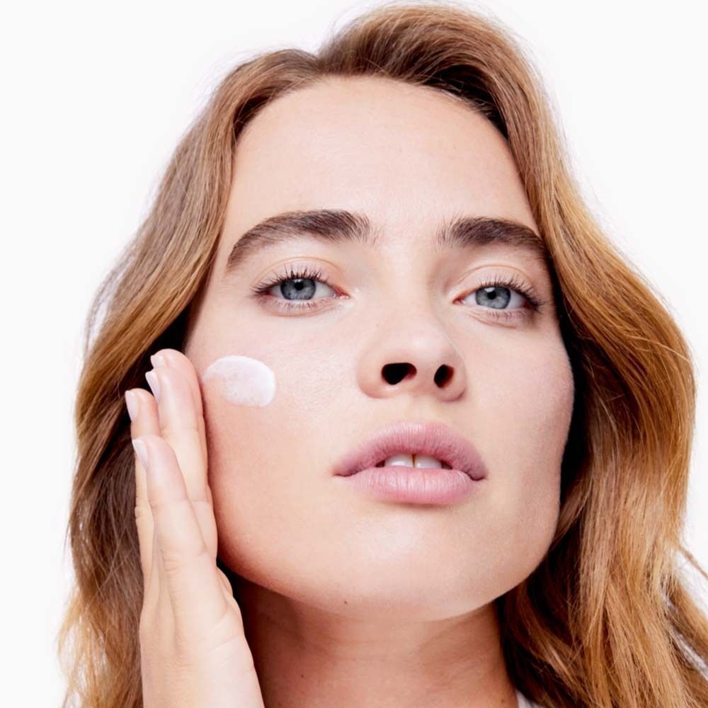 Nahaufnahme einer Frau, die Creme auf ihr Gesicht aufträgt. Heller Hintergrund.
