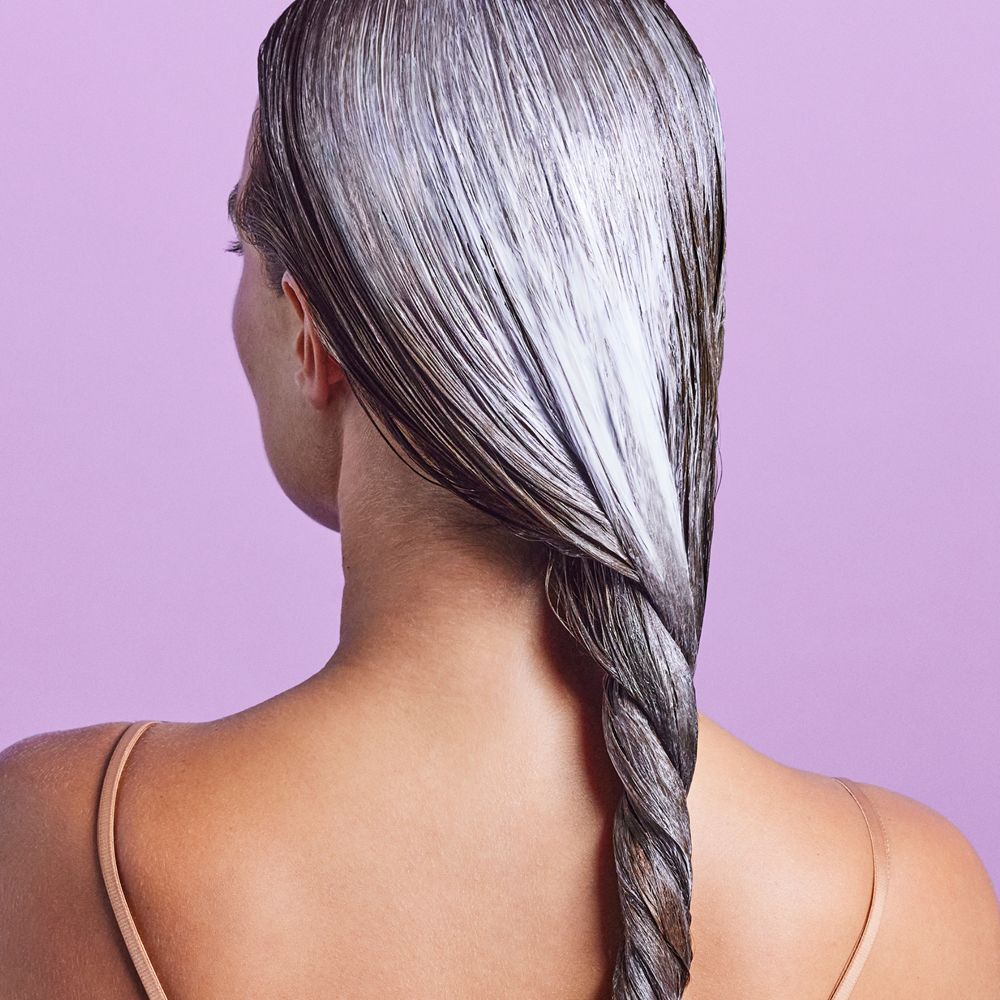 Rückansicht einer Person mit feuchtem Haar. Das Haar ist mit einer weißen Substanz bedeckt und zu einem Zopf geflochten.