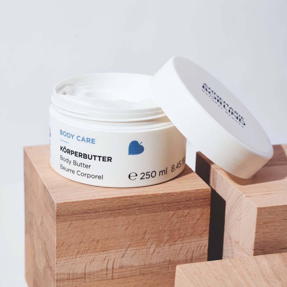 Offener weißer Tiegel mit Körperbutter auf Holzsockeln.