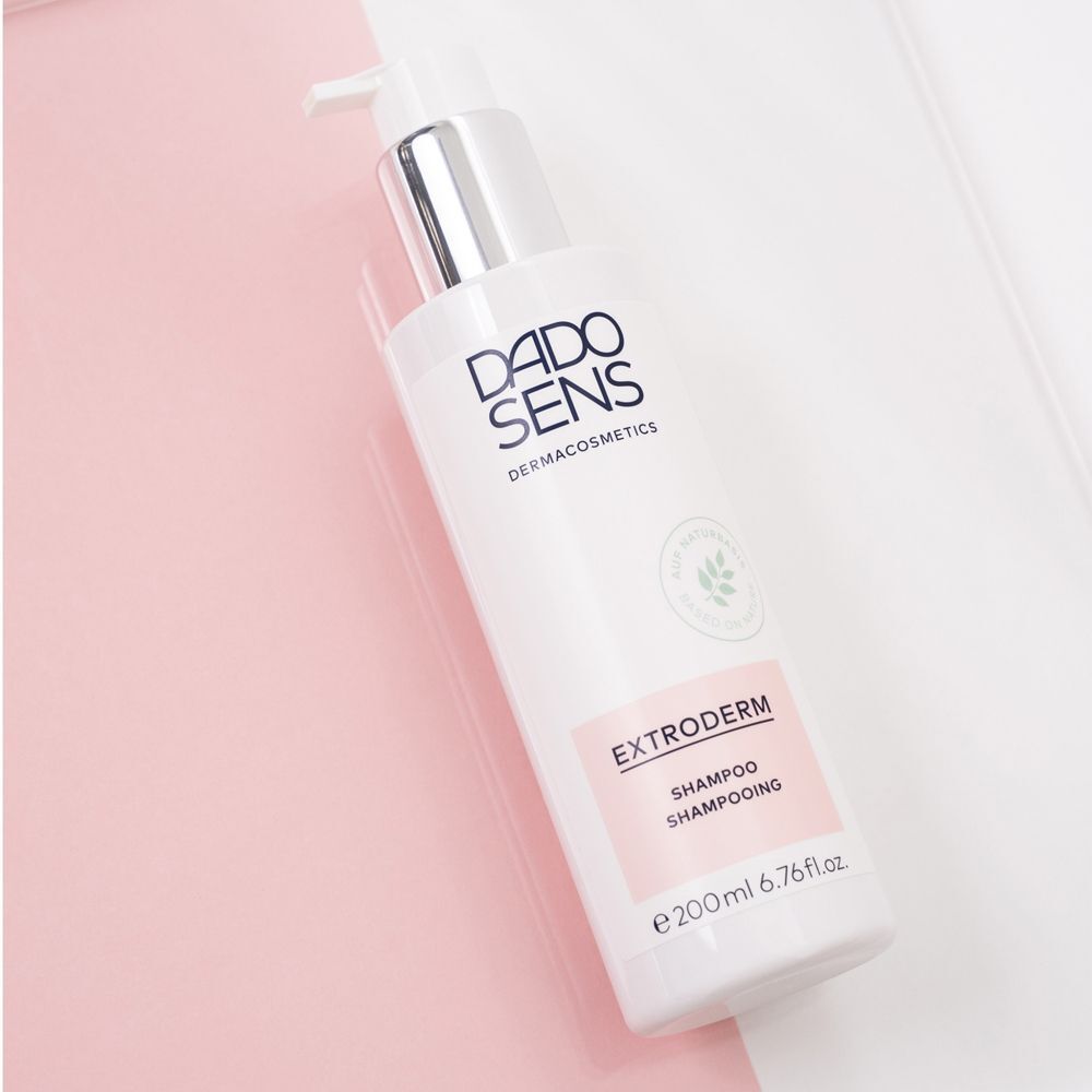 Weiße Pumpflasche DADO SENS EXTRODERM Shampoo auf rosa und weißem Hintergrund.