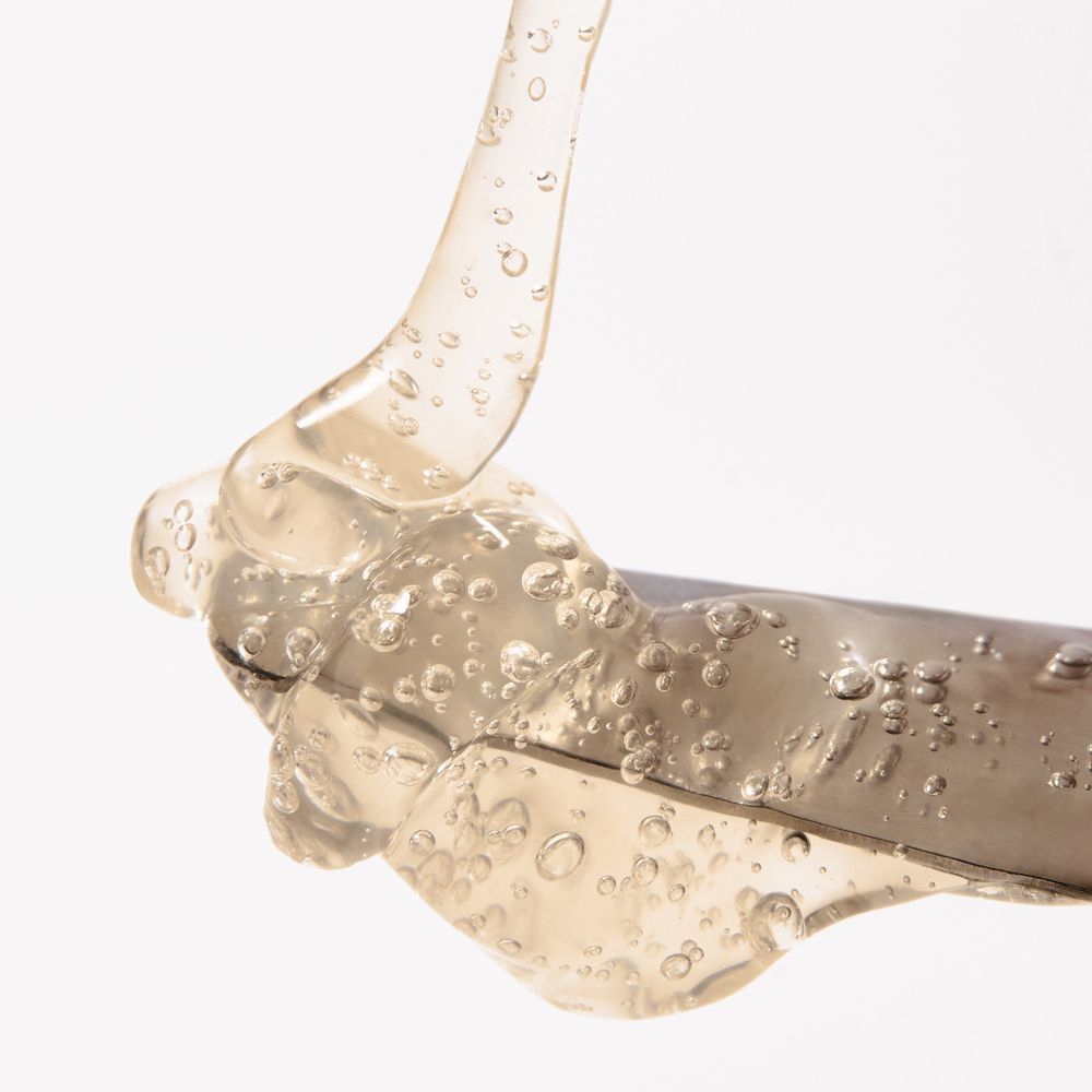 Nahaufnahme einer transparenten, gelartigen Substanz mit Bläschen, die von einem Metallwerkzeug tropft.