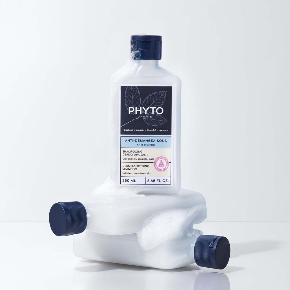 Eine Shampoo-Flasche auf einer anderen, mit Schaum bedeckten Flasche. Blaue Deckel. Aufschrift: PHYTO PARIS, Anti-Juckreiz.