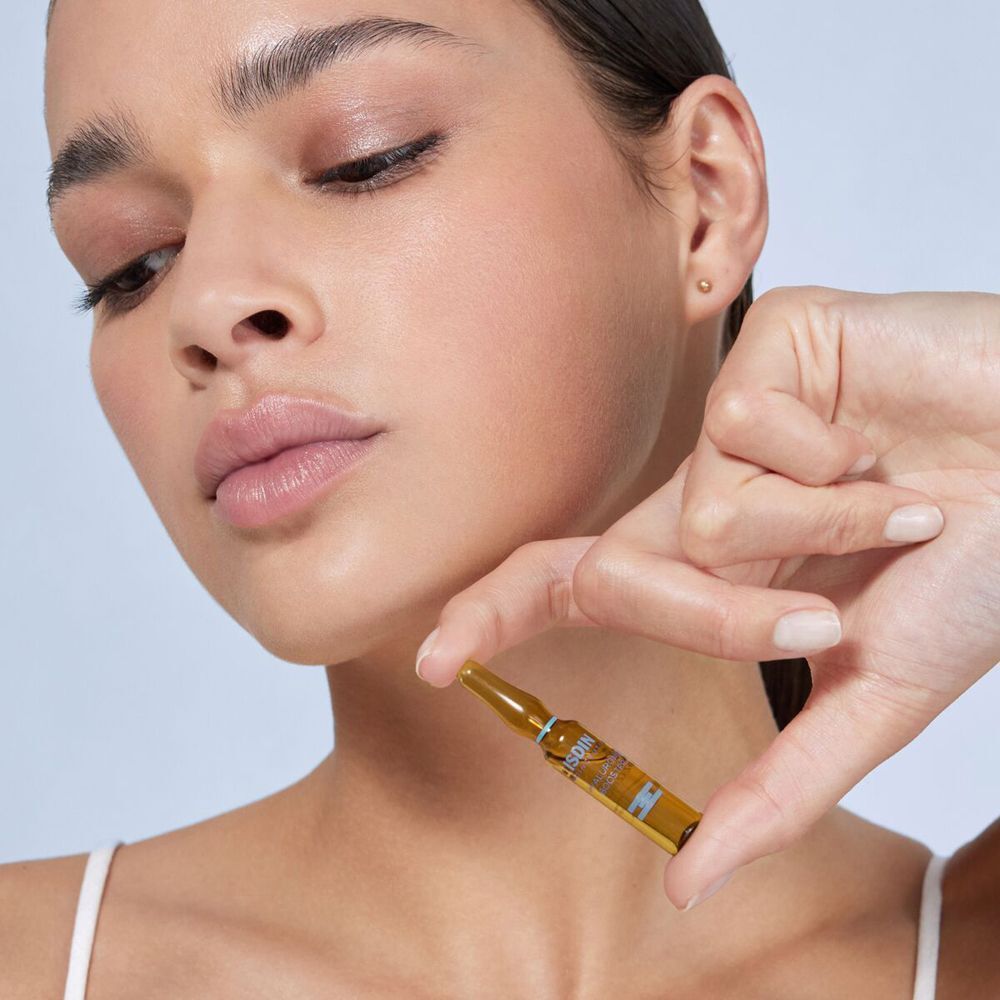 Frau hält eine Ampulle ISDINCEUTICS® Hyaluronic Booster. Die Ampulle ist braun und enthält eine Flüssigkeit.