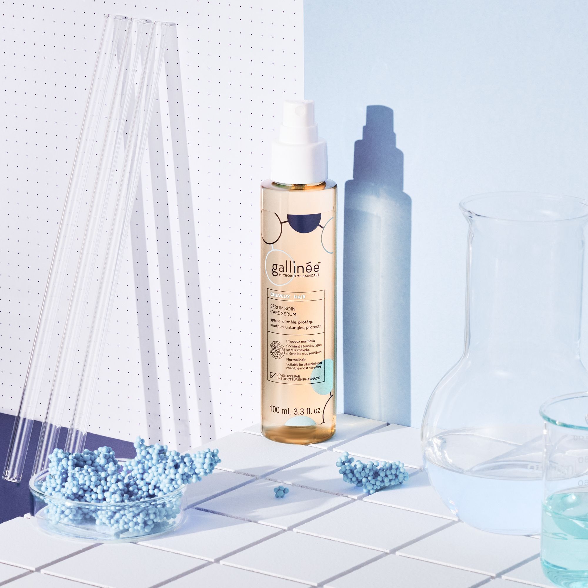 Eine Sprühflasche mit gelblicher Flüssigkeit. Aufschrift: gallinée, Sérum Soin Care Serum. Hintergrund: Laborutensilien und blaue Elemente.