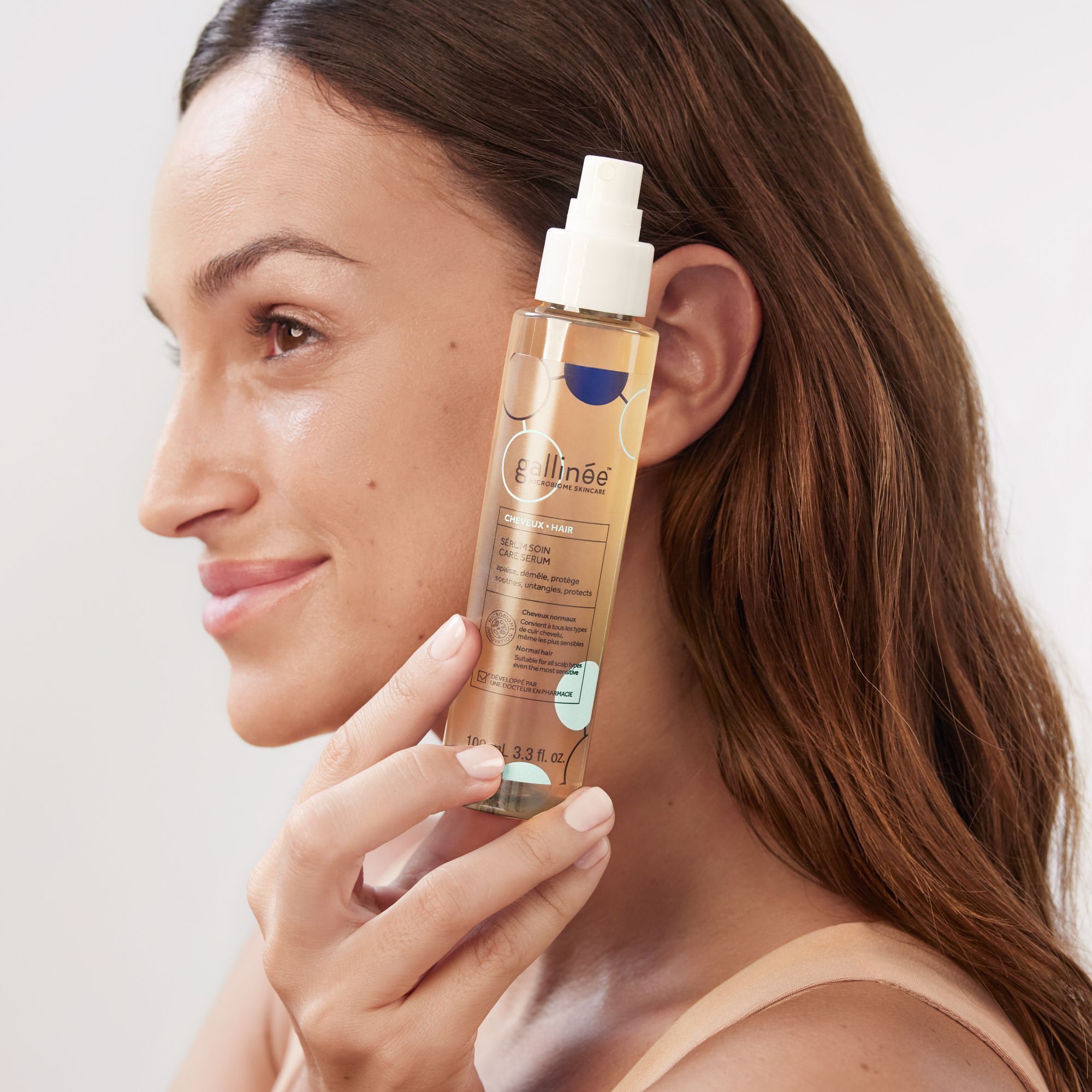 Frau hält eine Sprühflasche. Aufschrift: gallinée, Sérum Soin Care Serum. Frau mit braunen Haaren und beigem Oberteil.