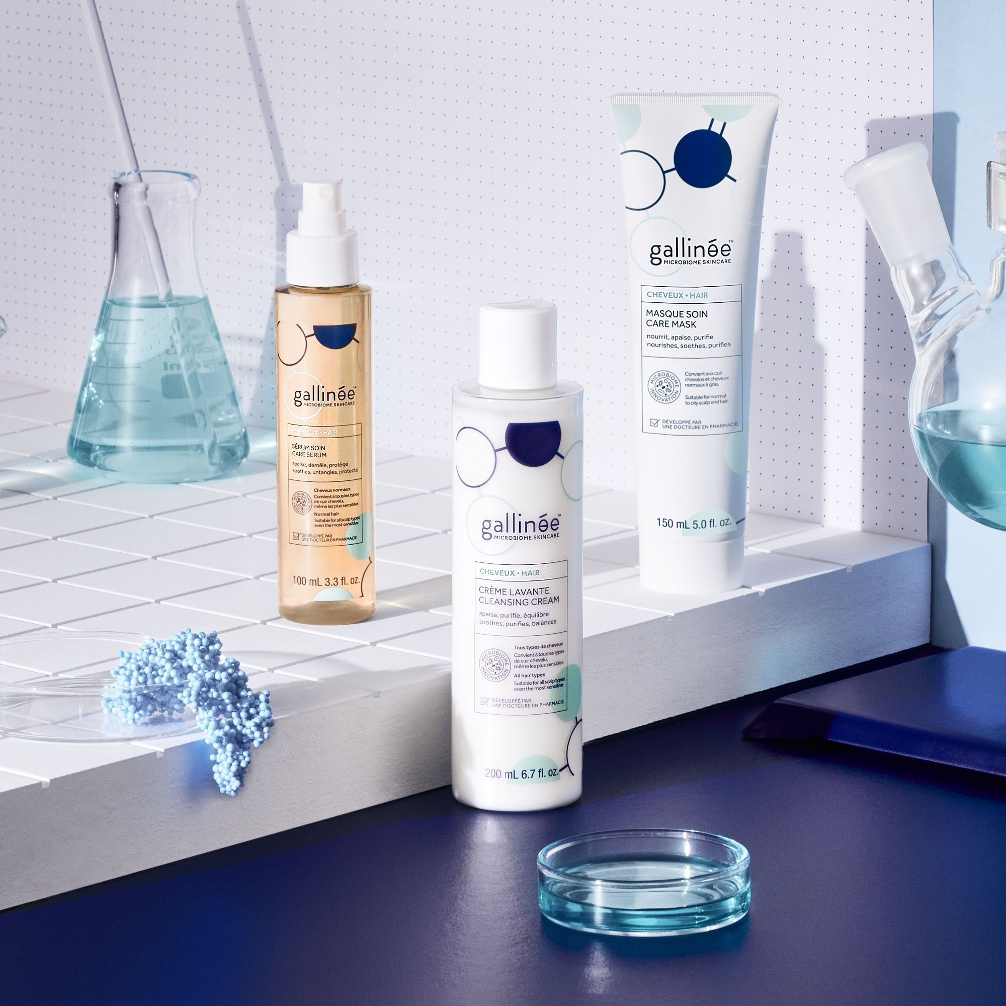 Drei Produkte: Sprühflasche, Flasche und Tube. Aufschrift: gallinée. Hintergrund: Laborutensilien und blaue Elemente.