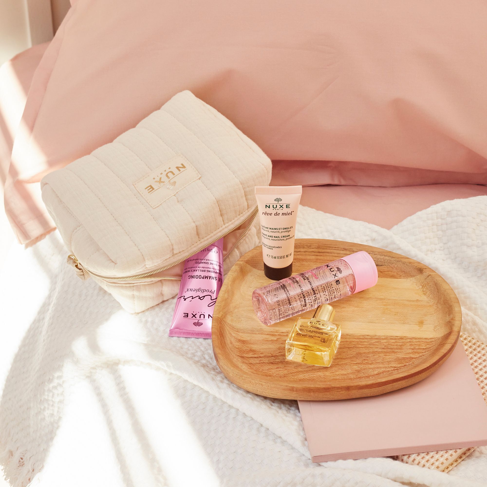 Kosmetiktasche mit NUXE-Produkten auf einem Holztablett. Enthalten sind Gesichtscreme, Trockenöl, Parfum und weitere Produkte.