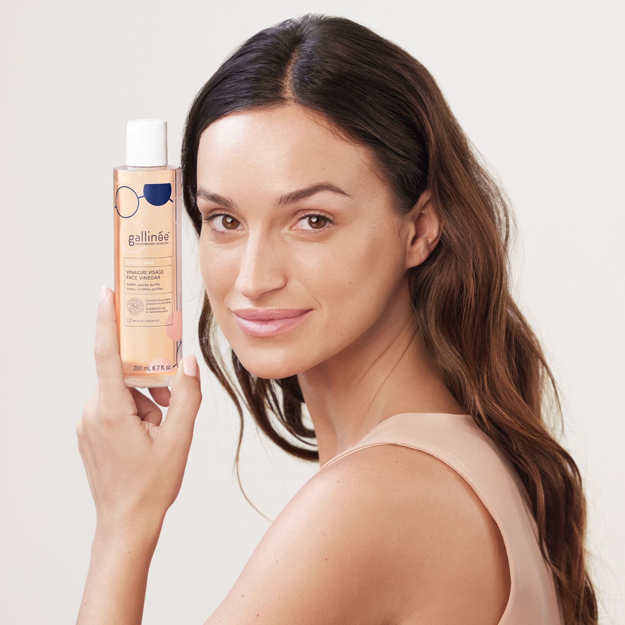 Frau hält eine Flasche. Aufschrift: Vinaigre Visage Face Vinegar. 200 ml. Frau mit langen braunen Haaren.