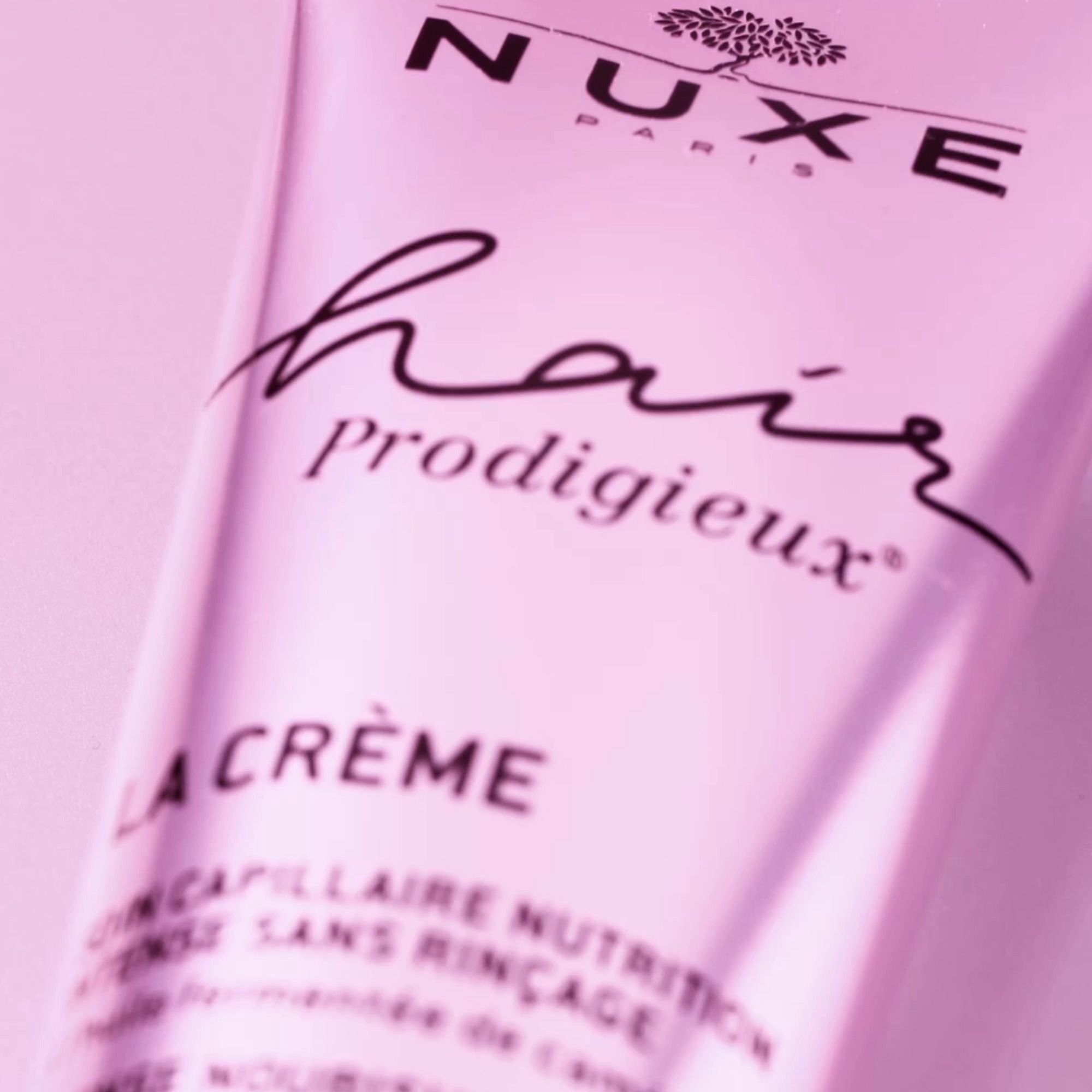 Nahaufnahme einer rosa Tube. Aufschrift: NUXE, Hair Prodigieux, LA CRÈME, Leave-in Creme. Mit Inhaltsstoffen aus fermentiertem rosa Kamelienöl.