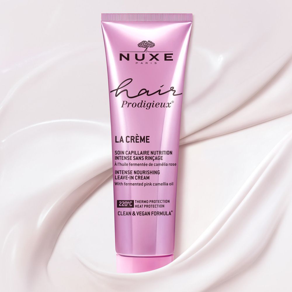 Rosa Tube auf weißem Stoff. Aufschrift: NUXE, Hair Prodigieux, LA CRÈME, Leave-in Creme. Mit Inhaltsstoffen aus fermentiertem rosa Kamelienöl.