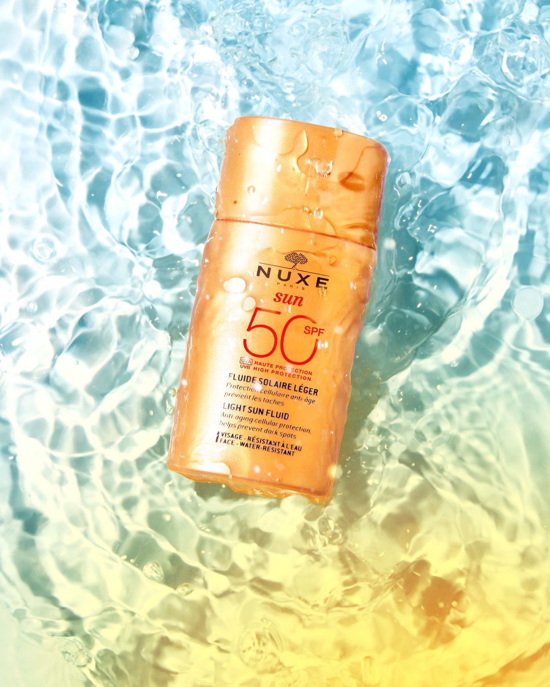 Sonnenfluid-Flasche im Wasser. Aufschrift: NUXE Sun, SPF 50, Fluide Solaire Léger, Anti-Aging-Schutz, hilft, dunkle Flecken zu verhindern.