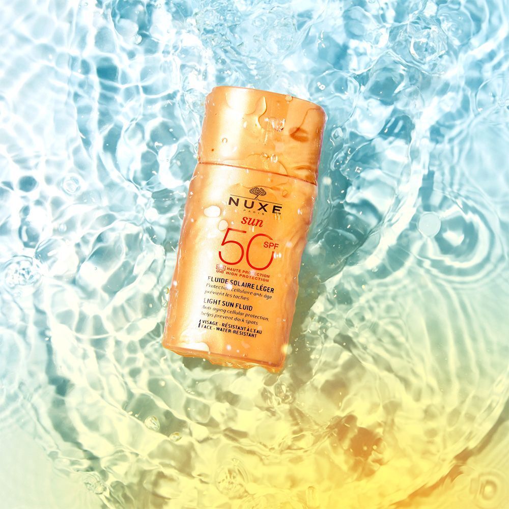 Sonnenfluid-Flasche im Wasser. Aufschrift: NUXE Sun, SPF 50, Fluide Solaire Léger, Anti-Aging-Schutz, hilft, dunkle Flecken zu verhindern.