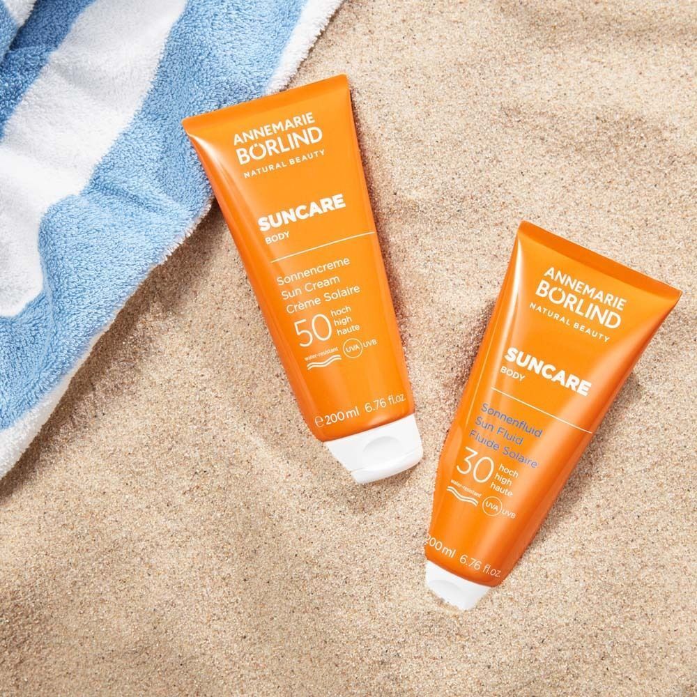 Zwei Tuben auf Sand. Eine mit LSF 50, die andere mit LSF 30. Aufschrift: SUNCAR, Sonnencreme, Sun Fluid.