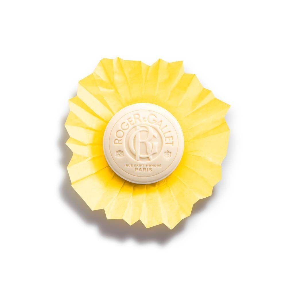 Runde, cremefarbene Seife in gelbem, gefaltetem Papier. Auf der Seife ist ein Logo und Schriftzug zu sehen.