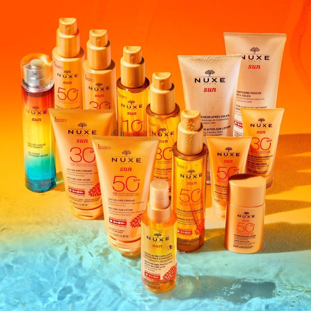 Verschiedene Produkte: Flakons, Tuben, Sprays. Text: NUXE Sun, 50, 30. Auf blau-orangefarbenem Hintergrund.