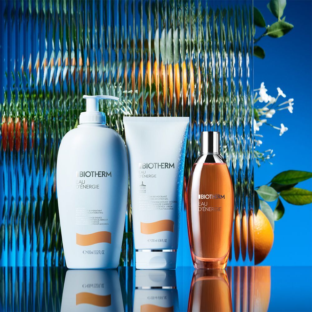 Drei BIOTHERM Eau d'Energie Produkte: Body Milk, Duschgel und Bodyspray. Auf blauem Hintergrund mit Obst.