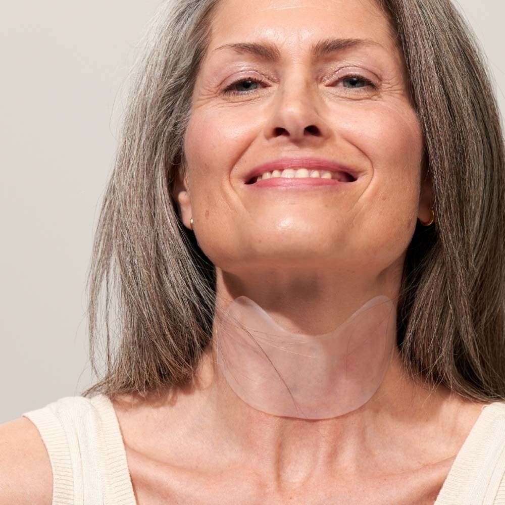 Frau mit grauen Haaren trägt ein transparentes Hals Pad. Das Pad bedeckt den Halsbereich.