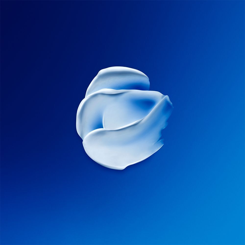 Nahaufnahme einer weißen Creme auf blauem Hintergrund. Die Creme ist in einer geschwungenen Form angeordnet.