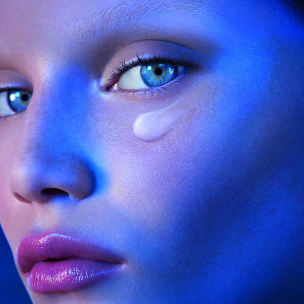 Nahaufnahme eines Gesichts mit blauen Augen und Lippen. Ein Tropfen Creme unter dem Auge.