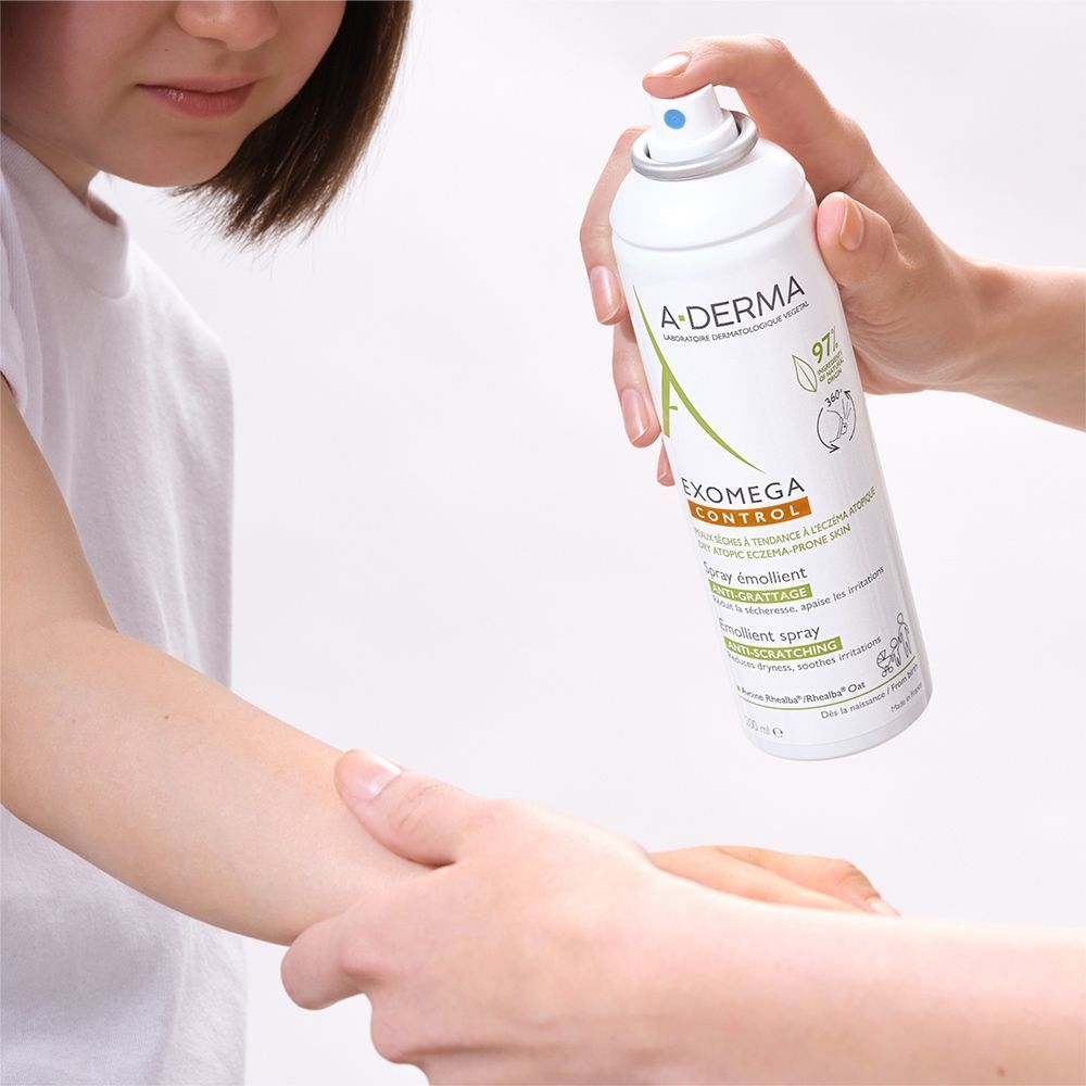 Person sprüht A-DERMA EXOMEGA CONTROL Spray auf den Arm einer anderen Person. Weiße Flasche mit grünem Deckel.