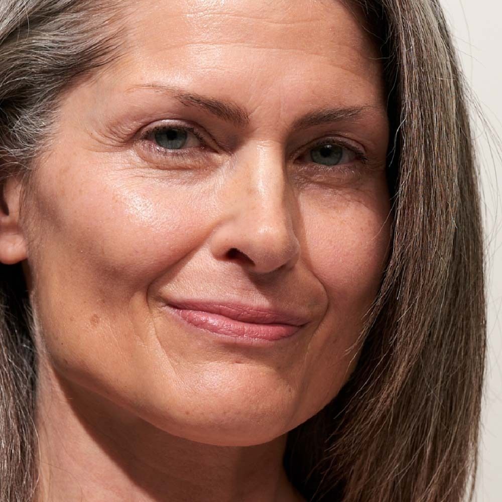 Nahaufnahme einer Frau mit grauem Haar. Sie lächelt leicht. Hautton ist hell.