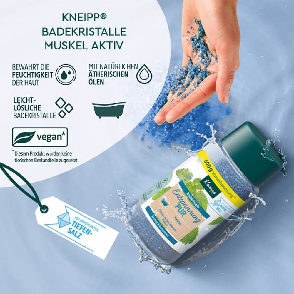 Eine Flasche KNEIPP Badekristalle wird in Wasser gehalten. Blaue Kristalle verteilen sich. Label mit Produktnamen und Logo.