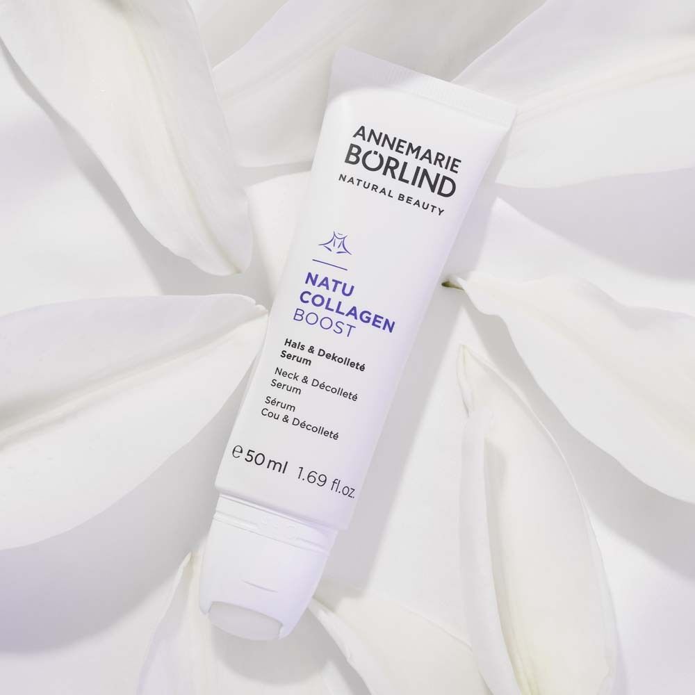 Eine Tube ANNEMARIE BÖRLIND Natu Collagen Boost Hals & Dekolleté Serum auf weißen Blütenblättern.