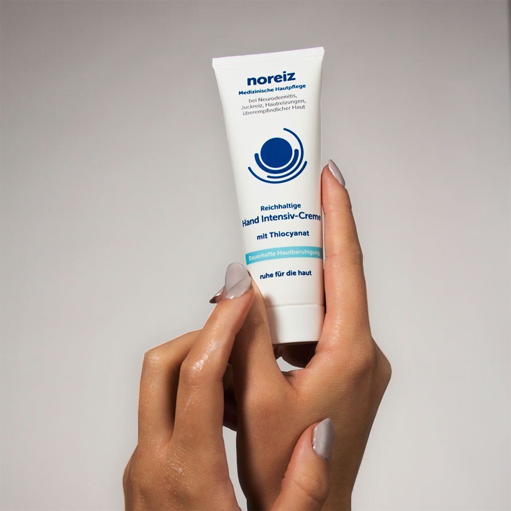 Weiße Tube mit blauer Beschriftung, gehalten von Händen. Aufschrift: Hand Intensiv-Creme, mit Thiocyanat. Medizinische Hautpflege. Logo: blauer Kreis mit Wellen.