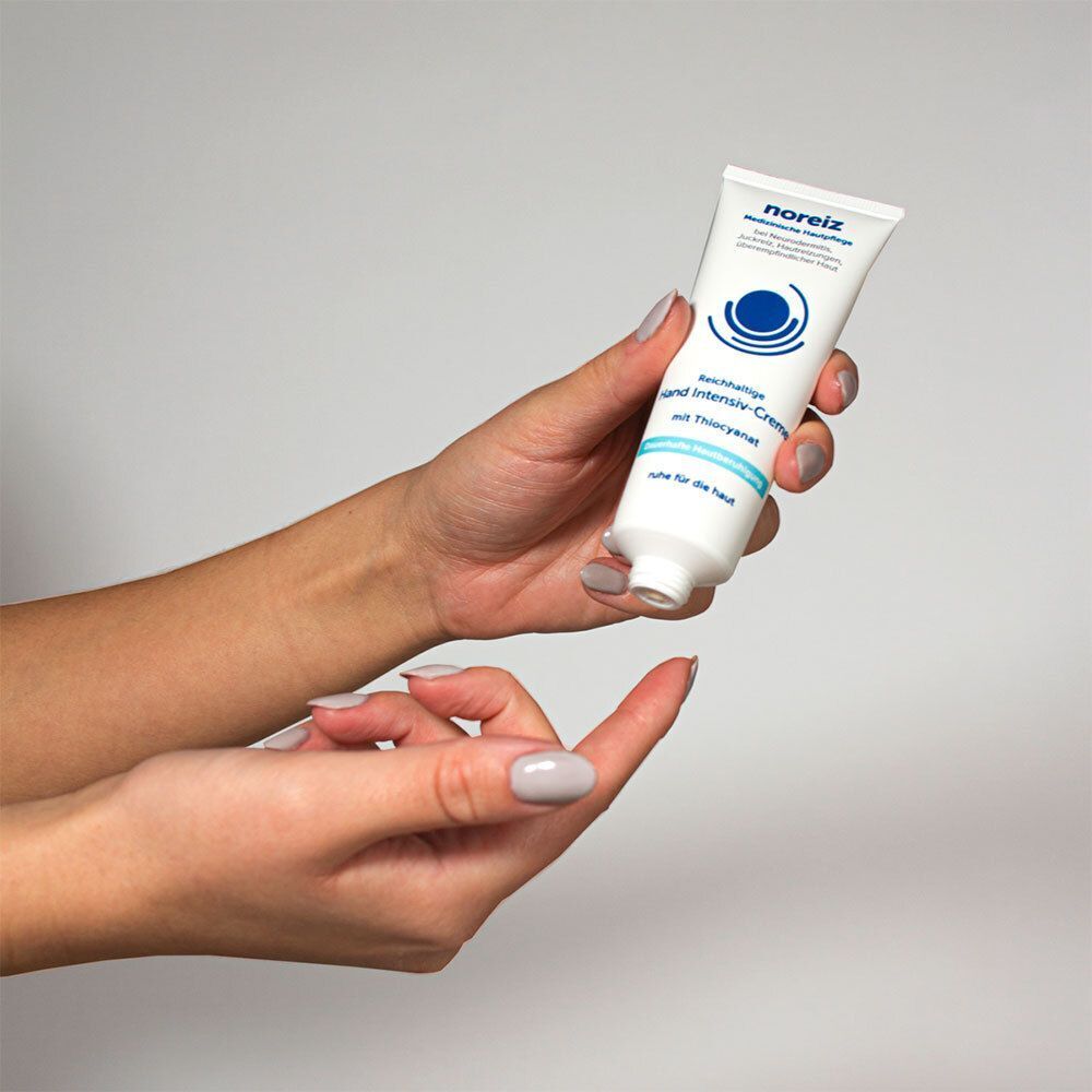 Weiße Tube mit blauer Beschriftung, gehalten von Händen. Aufschrift: Hand Intensiv-Creme, mit Thiocyanat. Medizinische Hautpflege. Logo: blauer Kreis mit Wellen.