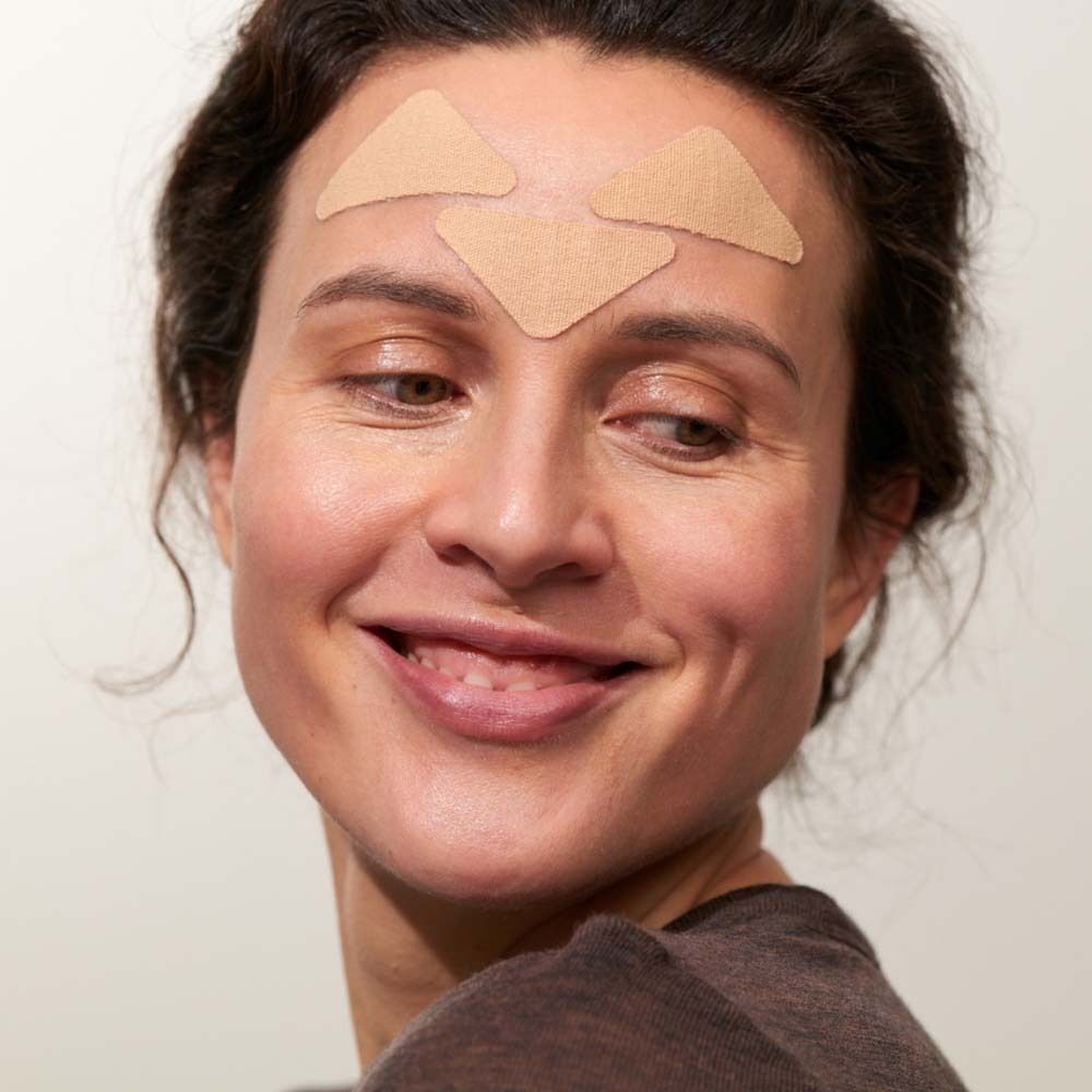 Frau mit drei dreieckigen Patches auf der Stirn. Die Patches sind beige und auf der Haut angebracht.