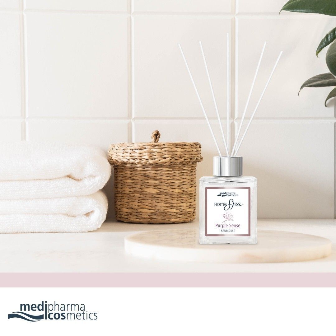 Raumduft-Set mit Flakon und Stäbchen. Aufschrift: HOME Spa Purple Sense Raumduft. Marke: medipharma cosmetics. Auf einem Tablett neben Handtüchern und Korb.