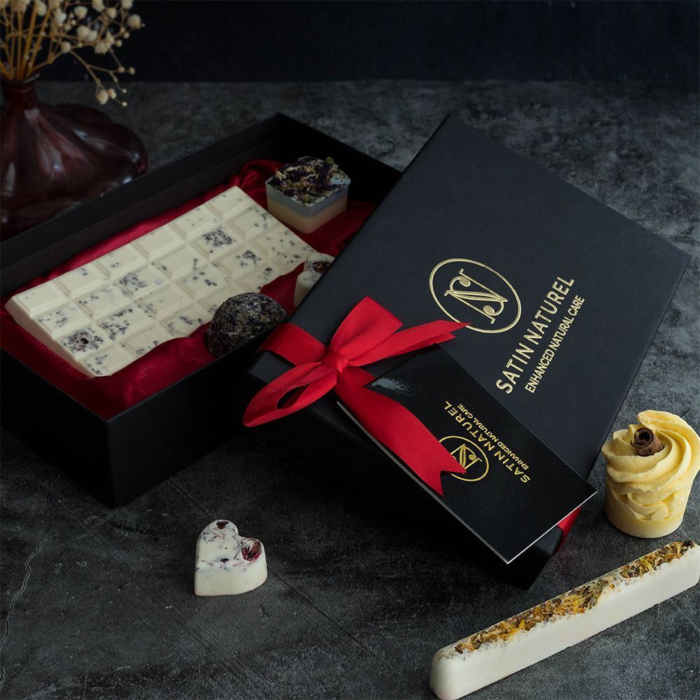 Schwarze Geschenkbox mit roter Schleife. Enthält Badepralinen in verschiedenen Formen. Logo: SATIN NATUREL. Visitenkarte.