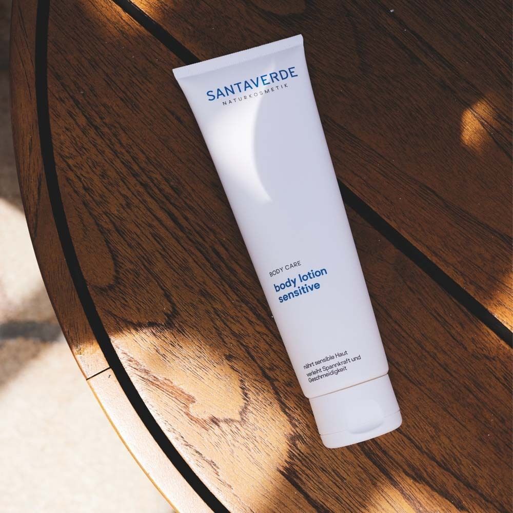 Weiße Tube SANTAVERDE Body Lotion sensitive auf Holzuntergrund. Blaue Schrift. Aufschrift: Body Care, sensitive. Naturkosmetik.