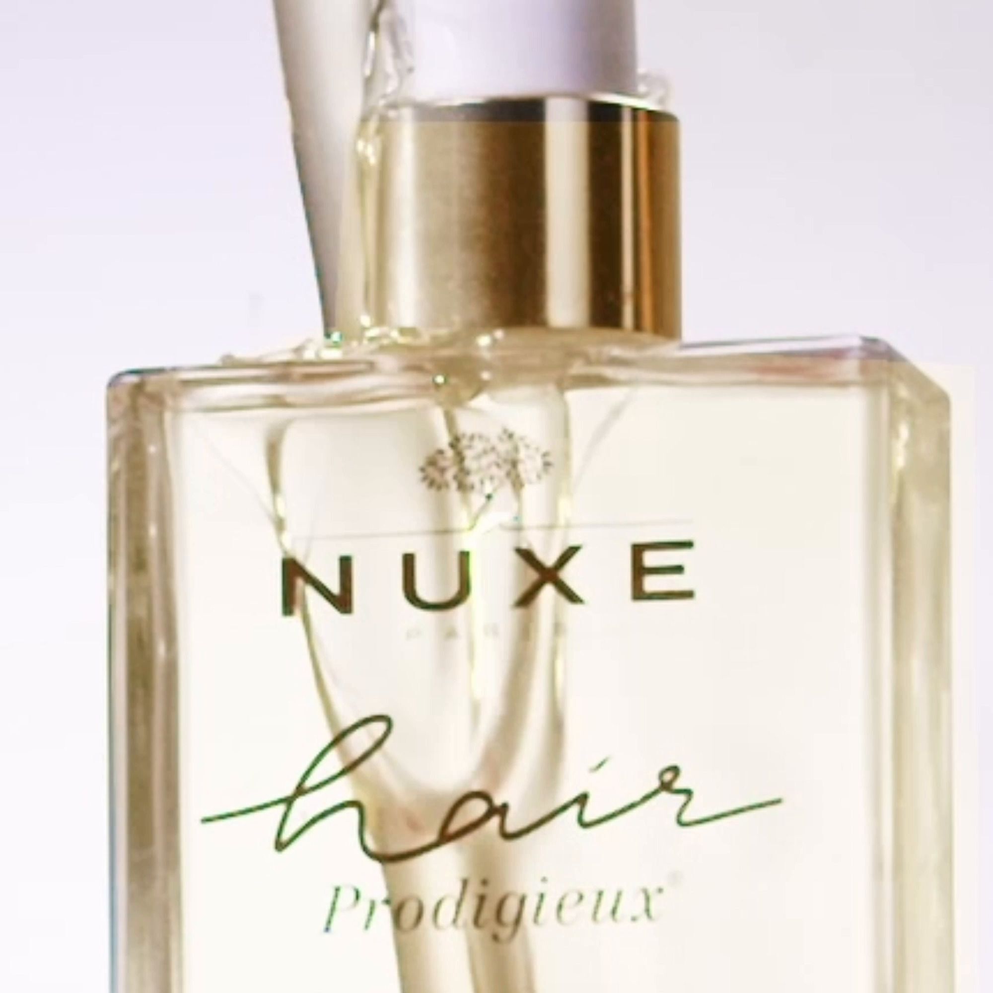 Nahaufnahme einer Flasche NUXE Hair Prodigieux. Klarer Behälter mit goldenem Deckel und weißer Pumpe. Logo und Produktname sichtbar.