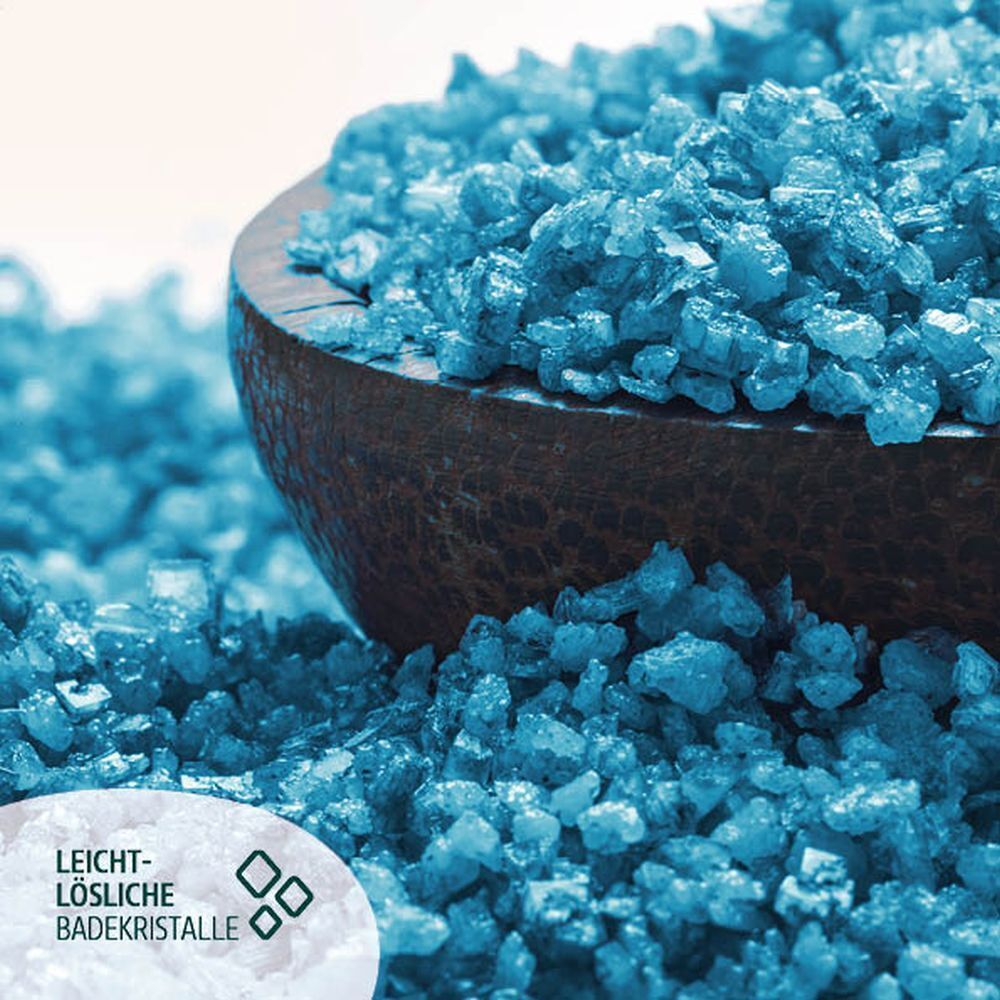 Nahaufnahme von blauen Badekristallen in einer Holzschale. Text: Leicht-lösliche Badekristalle.