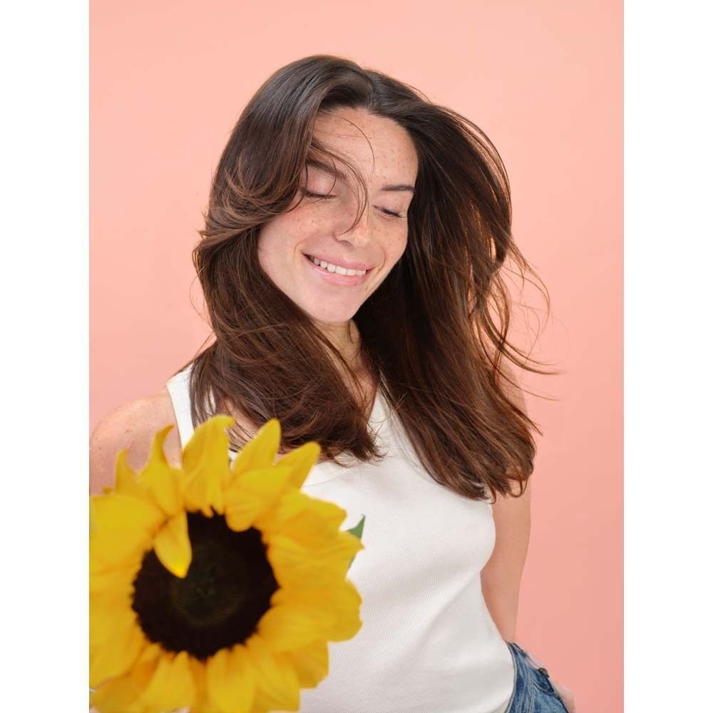 Eine Frau mit langen, braunen Haaren und einem Sonnenblumen. Sie lächelt und hält die Blume.